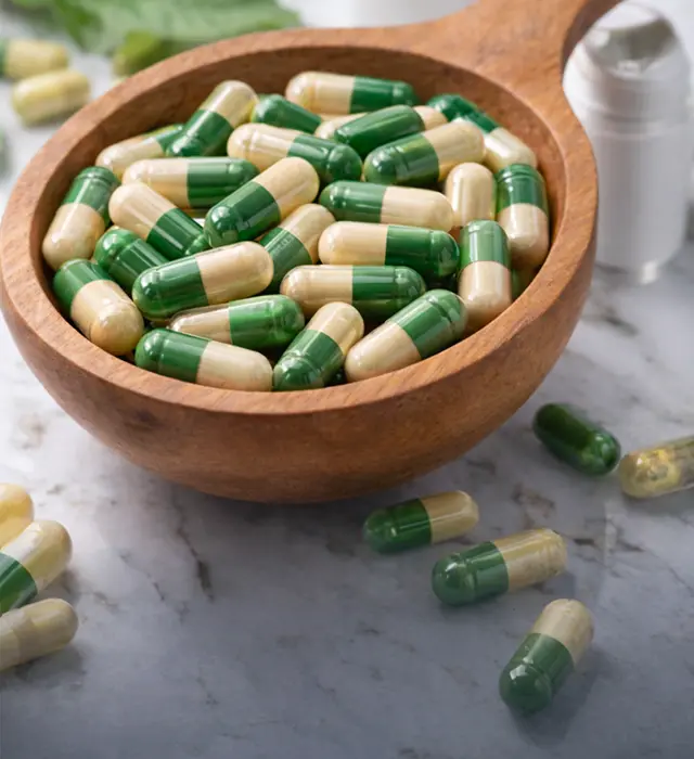 capsule supplement manufacturing with green and beige capsules in wooden bowl
